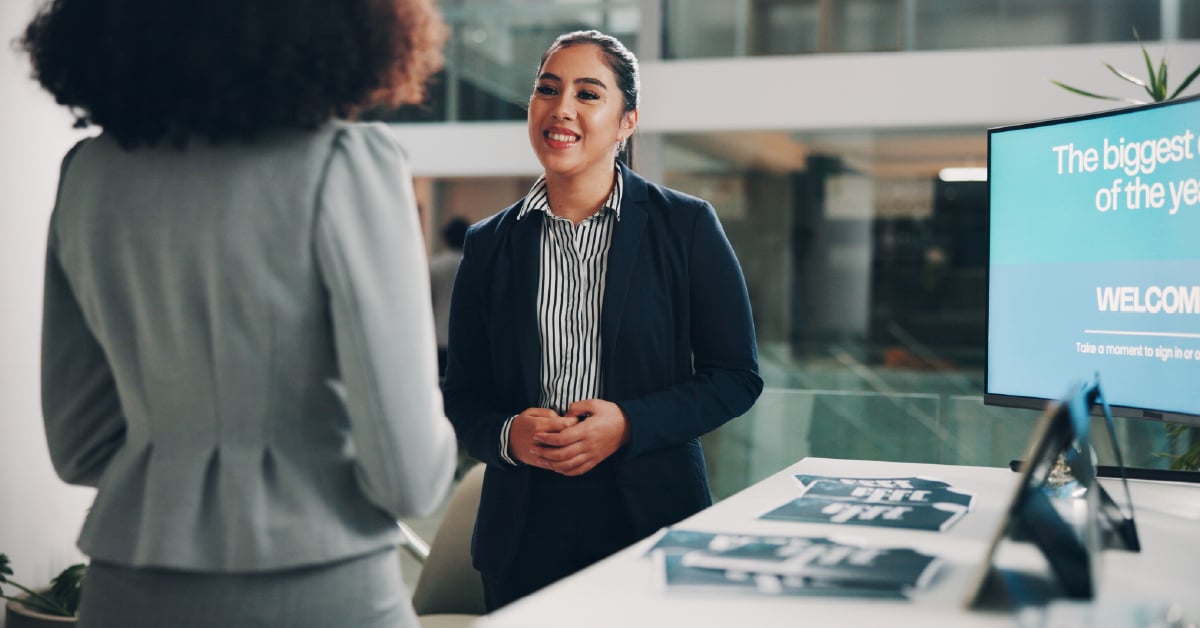 Woman in a blazer smiling while presenting to a colleague in front of a screen