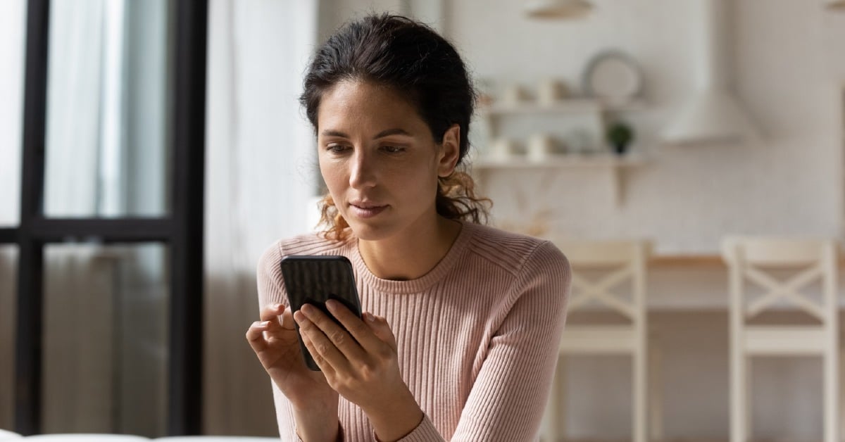 Woman standing in a kitchen looking down at her smartphone